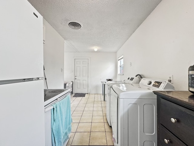 clothes washing area with separate washer and dryer, light tile patterned floors, and a textured ceiling