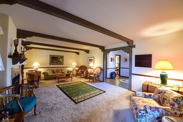 carpeted living room with beam ceiling, ornate columns, and a fireplace