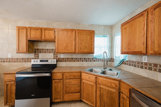 kitchen with sink, tile countertops, a textured ceiling, decorative backsplash, and appliances with stainless steel finishes