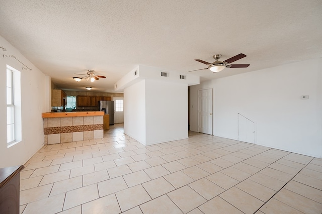 unfurnished living room featuring ceiling fan, light tile patterned floors, and a textured ceiling