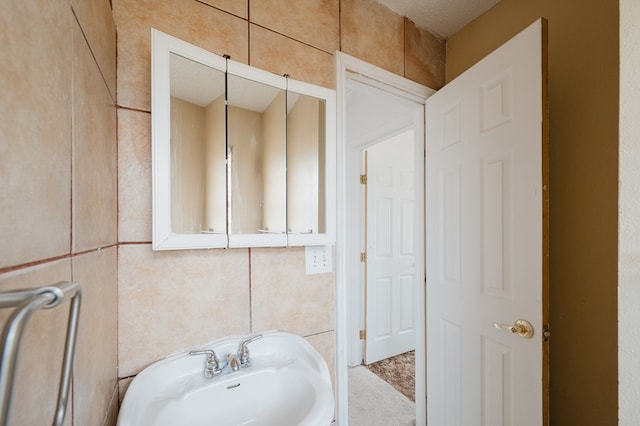 bathroom featuring a textured ceiling, sink, and tile walls