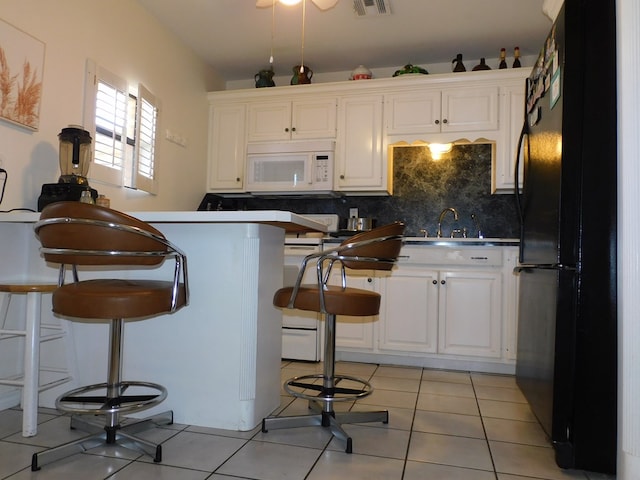 kitchen featuring black refrigerator, tasteful backsplash, sink, light tile patterned floors, and white cabinetry