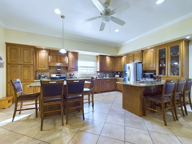 kitchen with appliances with stainless steel finishes, a kitchen island, light stone counters, and decorative light fixtures