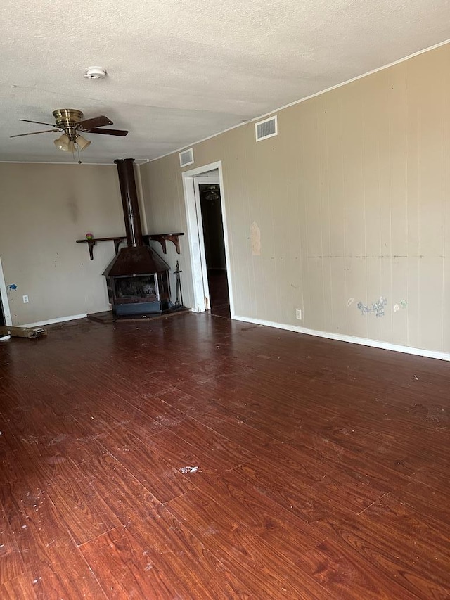 unfurnished living room featuring ceiling fan, a wood stove, a textured ceiling, and dark hardwood / wood-style flooring