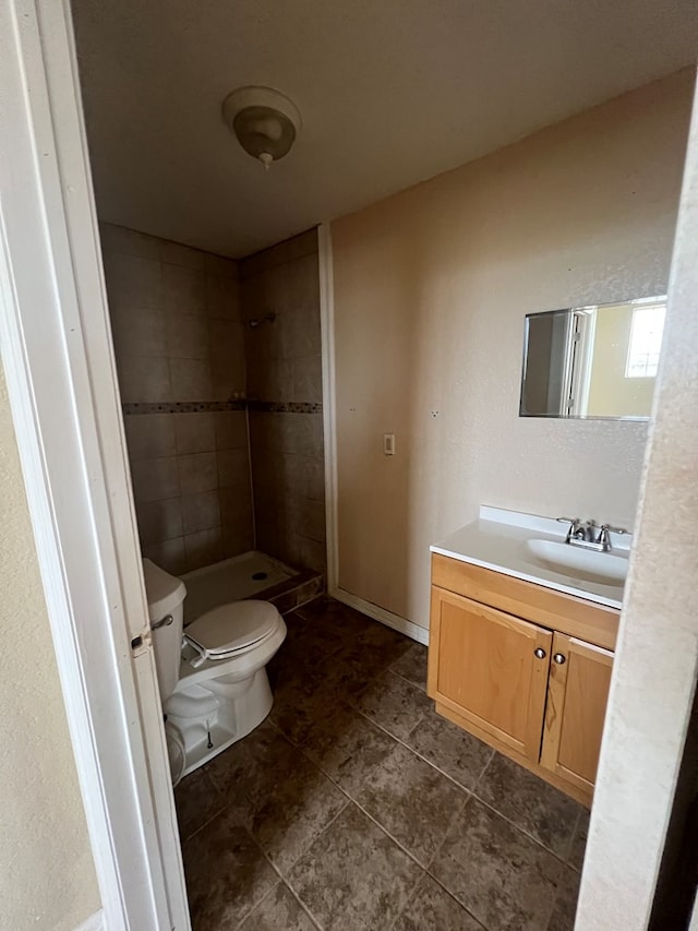 bathroom featuring tiled shower, tile patterned floors, vanity, and toilet