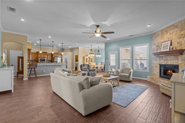 living area featuring dark wood-style floors, visible vents, a fireplace, ornamental molding, and ceiling fan