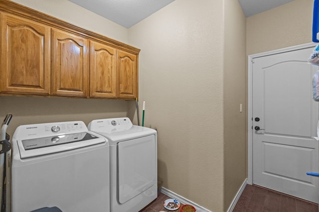 washroom featuring dark wood finished floors, cabinet space, washing machine and dryer, and baseboards