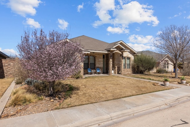 view of front of house with stone siding, a shingled roof, and a front yard