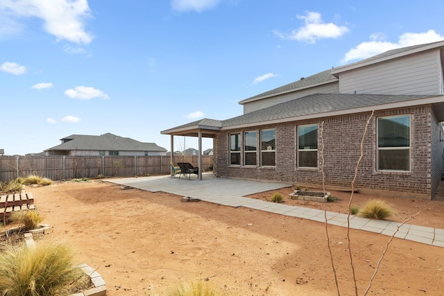 exterior space featuring brick siding, a fenced backyard, roof with shingles, and a patio