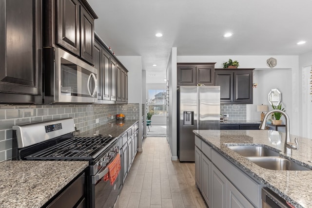 kitchen with light stone counters, backsplash, appliances with stainless steel finishes, dark brown cabinetry, and a sink