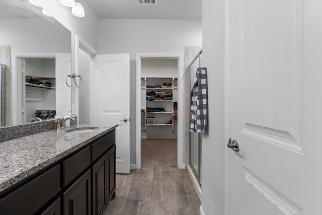 bathroom featuring a walk in closet, a shower stall, vanity, and wood finished floors