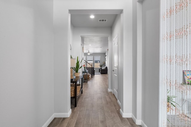 hallway featuring stairs, visible vents, baseboards, and wood finished floors