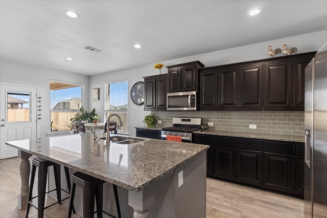 kitchen featuring a breakfast bar, visible vents, decorative backsplash, appliances with stainless steel finishes, and a sink