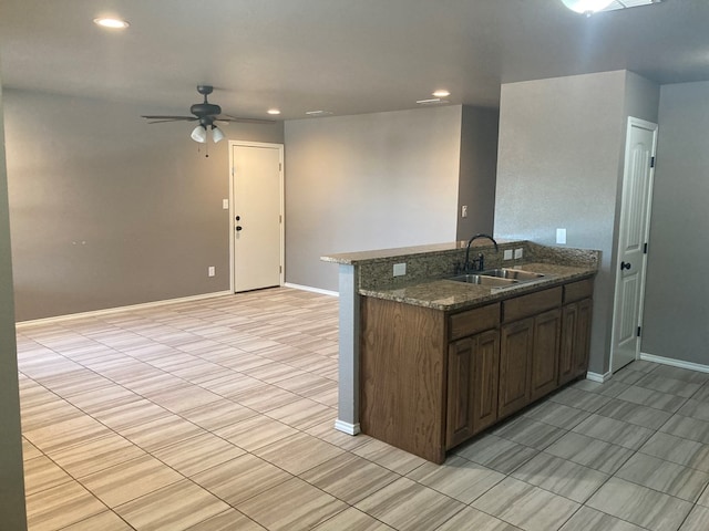 kitchen featuring kitchen peninsula, ceiling fan, dark stone countertops, and sink