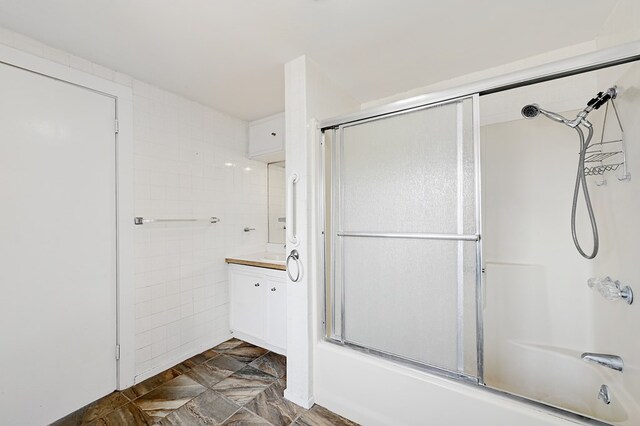 bathroom with vanity, tile walls, and bath / shower combo with glass door