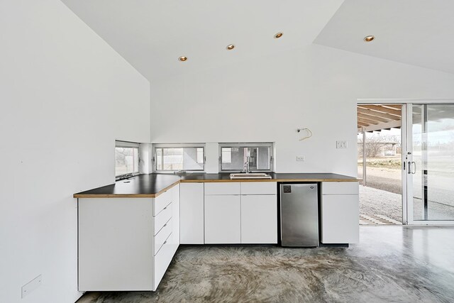 kitchen with stainless steel refrigerator, white cabinetry, kitchen peninsula, and a healthy amount of sunlight