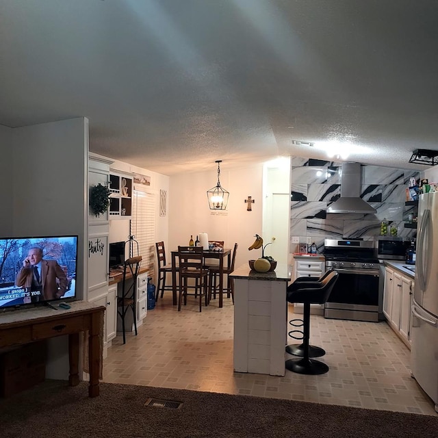 kitchen with hanging light fixtures, range hood, a kitchen bar, white cabinets, and appliances with stainless steel finishes