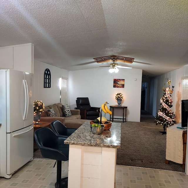 kitchen featuring a textured ceiling, ceiling fan, white refrigerator, stone countertops, and white cabinetry