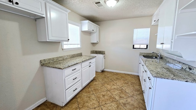 kitchen with sink, light tile patterned floors, a textured ceiling, light stone counters, and white cabinetry