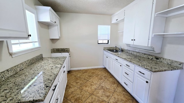 kitchen featuring light stone countertops, a textured ceiling, white cabinetry, and sink