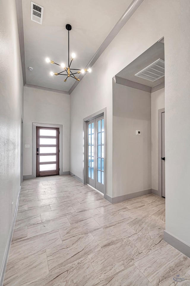 empty room featuring crown molding, french doors, a towering ceiling, and a notable chandelier