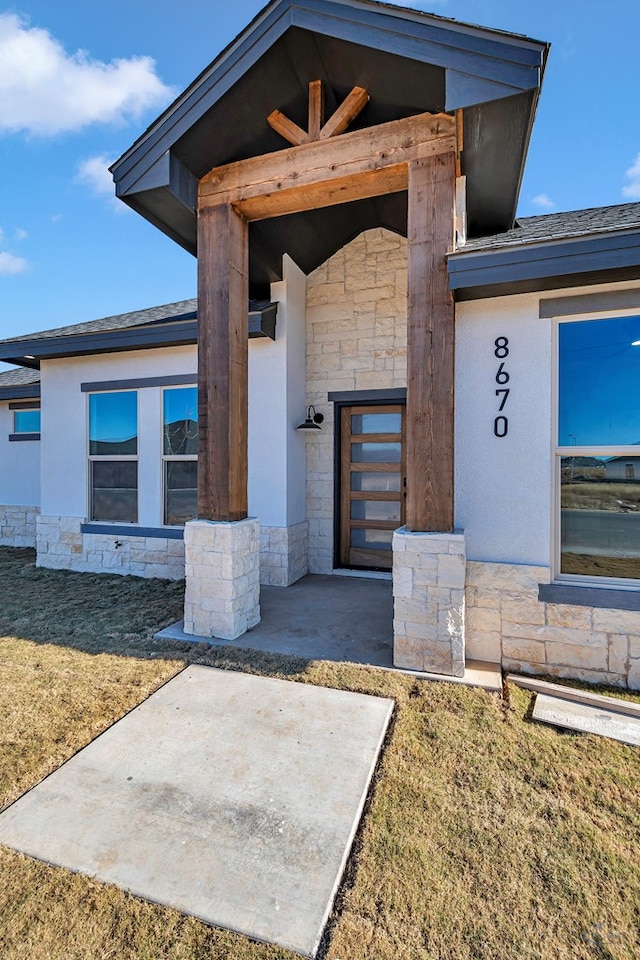 view of exterior entry with a lawn and a patio