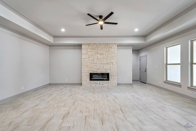 unfurnished living room with a fireplace, a tray ceiling, and ceiling fan