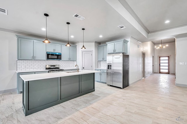 kitchen featuring decorative backsplash, stainless steel appliances, a kitchen island with sink, sink, and hanging light fixtures