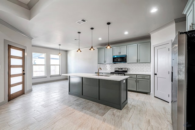 kitchen with pendant lighting, a kitchen island with sink, sink, decorative backsplash, and appliances with stainless steel finishes