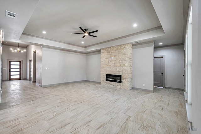 unfurnished living room with ceiling fan with notable chandelier, a tray ceiling, a stone fireplace, and crown molding