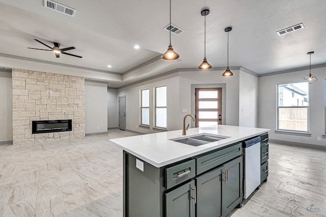 kitchen featuring dishwasher, a stone fireplace, sink, hanging light fixtures, and an island with sink