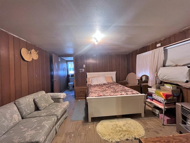 bedroom featuring a textured ceiling, light wood-type flooring, ensuite bathroom, and wood walls