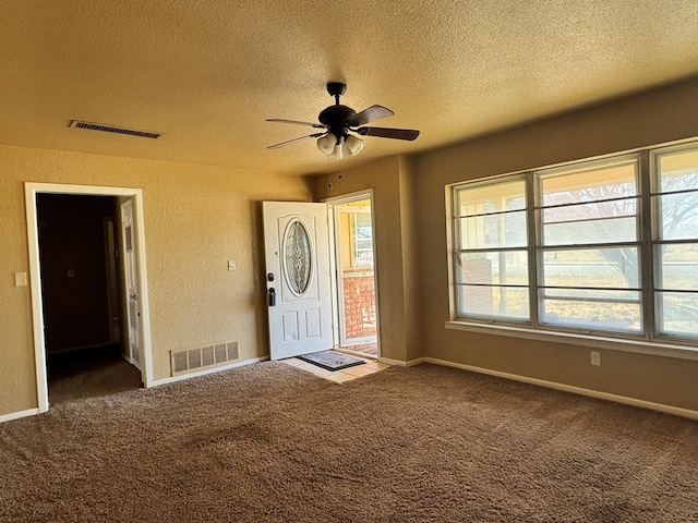 foyer entrance with baseboards, visible vents, a textured ceiling, and carpet flooring