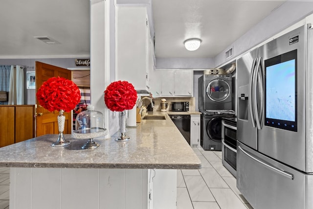 kitchen featuring a peninsula, a sink, white cabinetry, stacked washer / drying machine, and black appliances