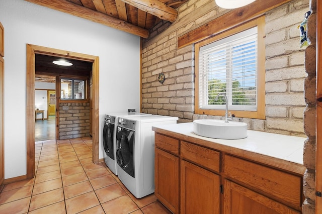 laundry room featuring light tile patterned flooring, brick wall, sink, and washing machine and dryer