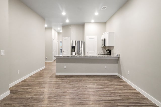 kitchen with wood finished floors, visible vents, a peninsula, stainless steel appliances, and white cabinets