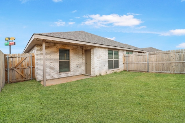 rear view of property featuring a fenced backyard, a yard, a shingled roof, brick siding, and a patio area