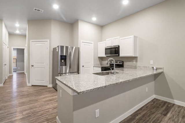 kitchen with light stone counters, appliances with stainless steel finishes, a peninsula, dark wood-style floors, and white cabinets