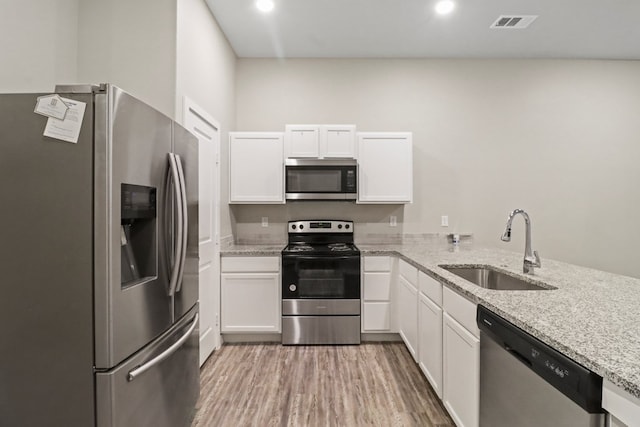 kitchen featuring visible vents, light wood-style flooring, stainless steel appliances, white cabinetry, and a sink