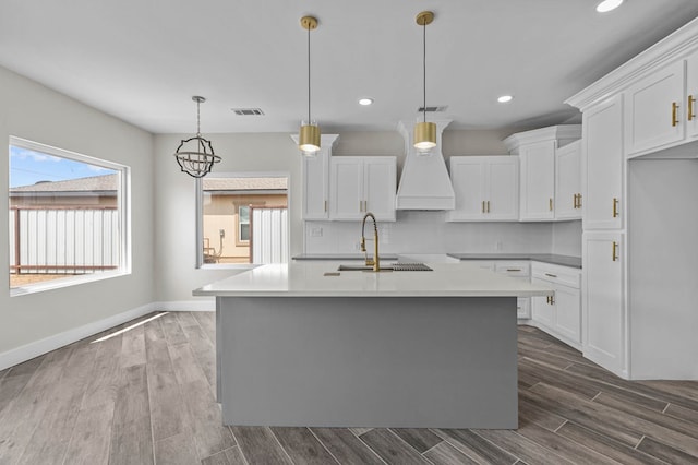 kitchen featuring a kitchen island with sink, white cabinets, and premium range hood