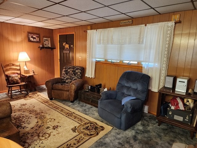 carpeted living area with wood walls and a drop ceiling