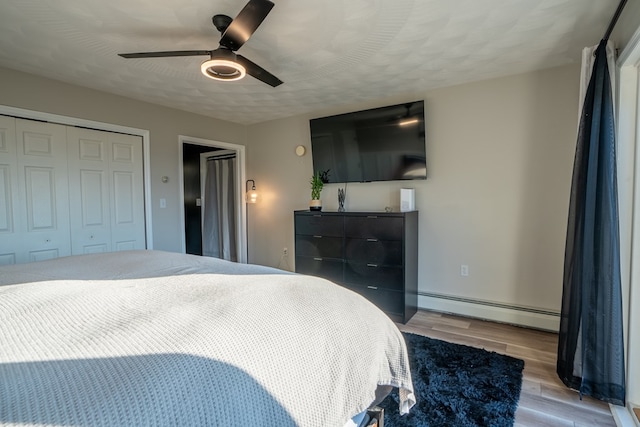 bedroom featuring light wood-type flooring, a closet, baseboard heating, and ceiling fan