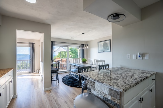 kitchen featuring white cabinetry, light hardwood / wood-style flooring, pendant lighting, and light stone counters