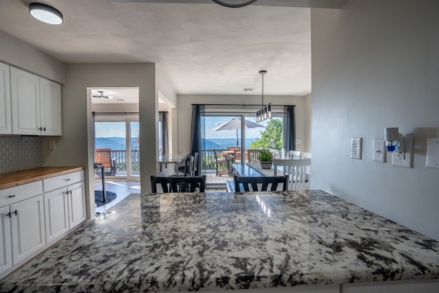 kitchen with a mountain view, wooden counters, white cabinets, hanging light fixtures, and tasteful backsplash