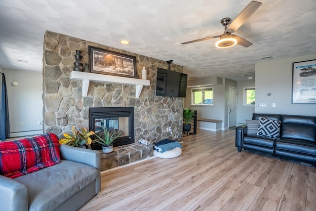 living room with a stone fireplace, ceiling fan, and hardwood / wood-style floors