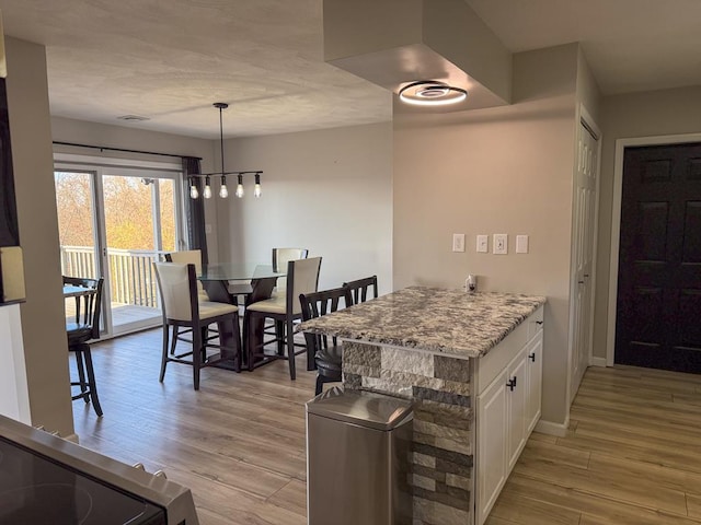 kitchen featuring hanging light fixtures, light stone counters, light hardwood / wood-style floors, white cabinets, and range