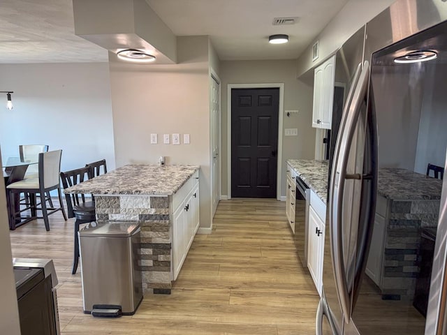 kitchen featuring appliances with stainless steel finishes, light hardwood / wood-style floors, white cabinetry, and light stone counters