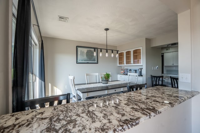 kitchen with light stone countertops, kitchen peninsula, white cabinetry, and pendant lighting