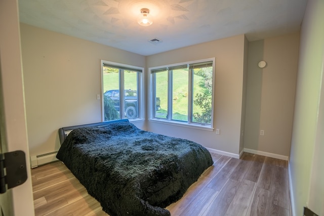 bedroom with baseboard heating and light hardwood / wood-style flooring