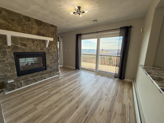 unfurnished living room featuring a stone fireplace, light wood-type flooring, and a baseboard radiator